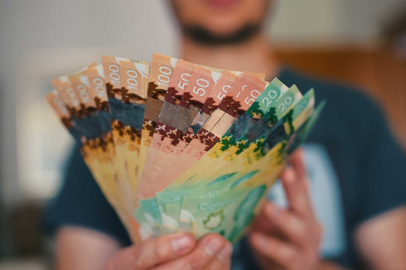 Hands passing a stack of Canadian dollar bills as a gift between family members, symbolizing tax-free giving in Canada.